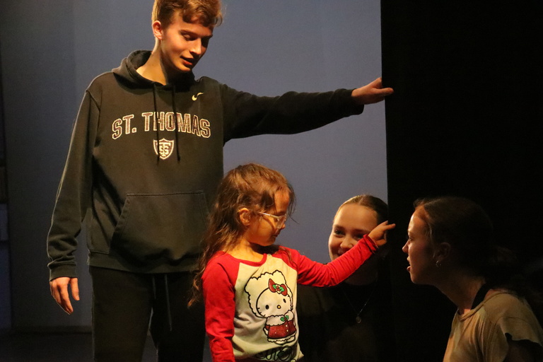 Six-year old EL student wearing a Hello Kitty shirt and pink glasses touches black curtain in Space Place theater as UIDC dancers Jack Delaney (behind in sweatshirt), Ruby Gentzler, and Madison Burkhart (kneeling) listen to her description of the curtain.