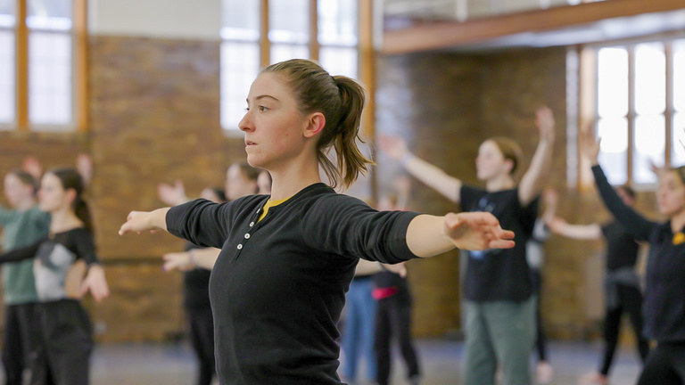 Sophia McLaughlin, an MFA in dance at the University of Iowa, with arms outstretched. She is with other UI dancers warming up to practice Martha Graham's Panorama.