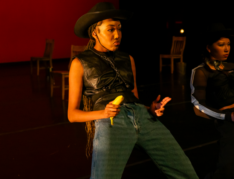 a dancer miming shooting guns from the hip, using bananas