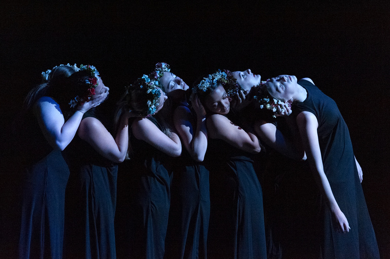 dancers clustered together, dimly lit on a darkened stage