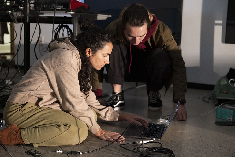 Two students working together on a laptop on the floor