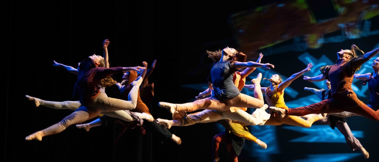 a group of dancers onstage at Dance Gala leaping in midair