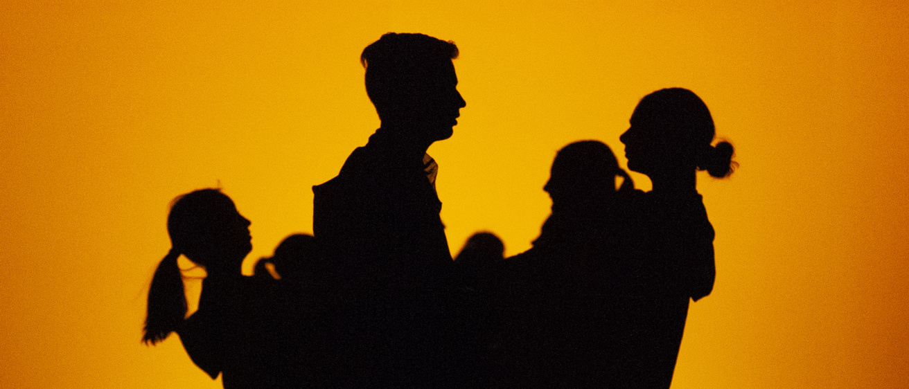 a group of dancers in a clump on stage in silhouette against a glowing orange background