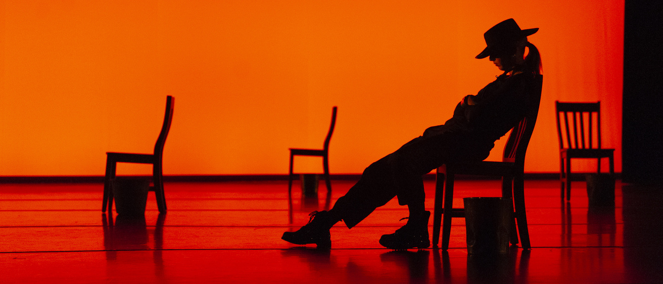 silhouette of a dancer in a cowboy hat laying over a chair against a red-lit background