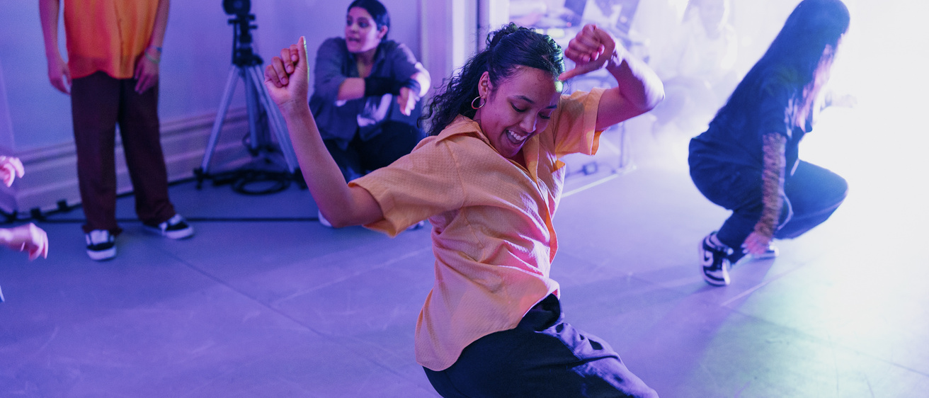 an exuberant youn woman dancer in street clothes, in a crouched position on her tiptoes in a house setting