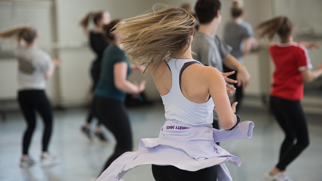 a group of undergraduate dancers in class in Halsey Hall. The main dancer in focus is shown from behind with her hair flying as she spins.