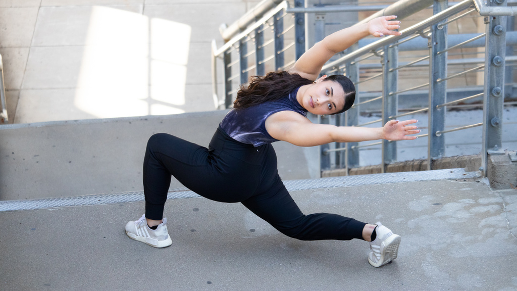 undergraduate student Ellie Daley dressed in black dancing on the steps of Catlett Hall. she is linging forward with her arms stretched over her head in the opposite direction and looking back at the camera
