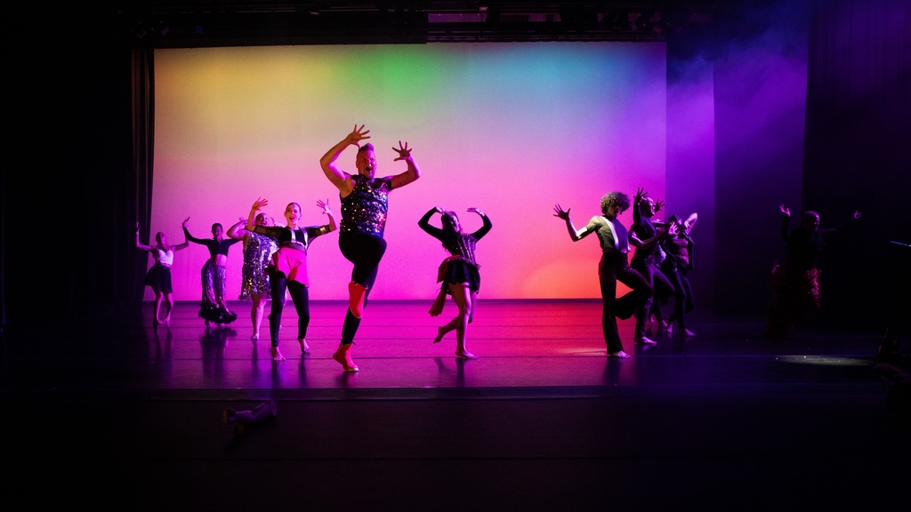 dancers in motion on stage against a rainbow background