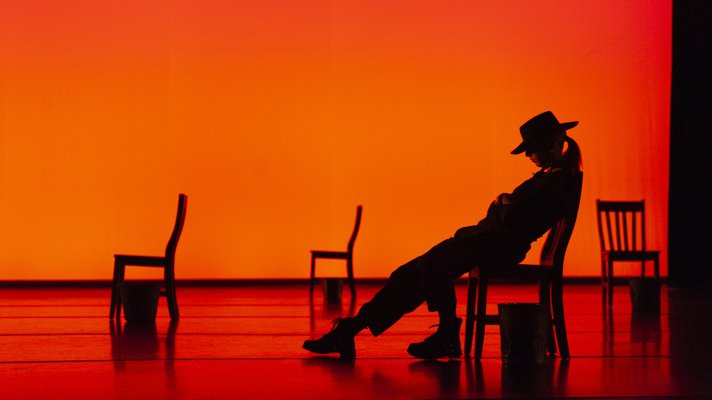 silhouette of a dancer in a cowboy hat laying over a chair against a red-lit background