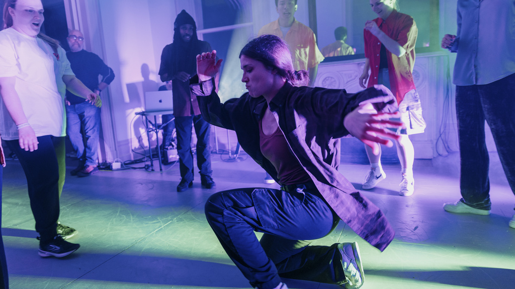 Emily Culbreath performing a low hip hop dance move in purple and green lighting at Public Space One